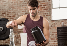 Various protein supplement containers with scoops and measuring cups on a wooden table