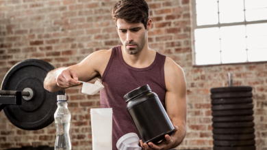 Various protein supplement containers with scoops and measuring cups on a wooden table