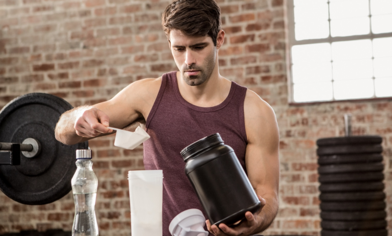 Various protein supplement containers with scoops and measuring cups on a wooden table